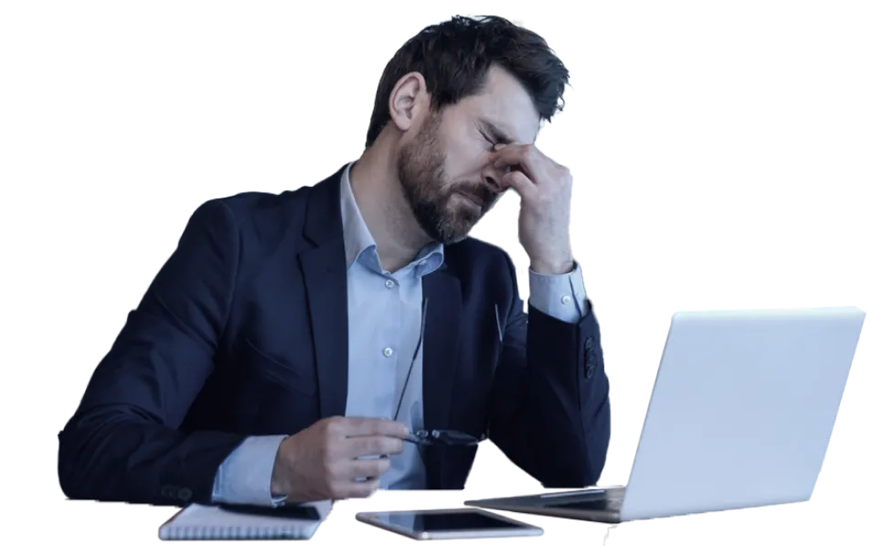 A man takes off his glasses and grabs the bridge of his nose out of frustration while sitting at a laptop.
